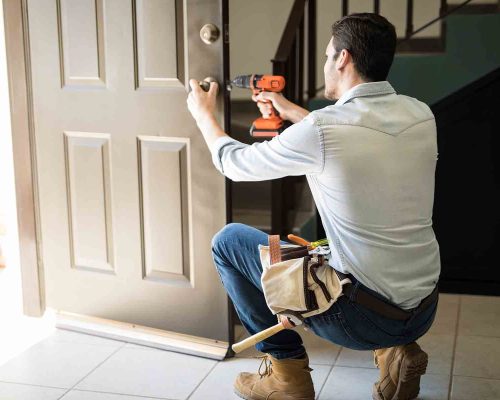 Rear view of a good looking man working as handyman and fixing a door lock in a house entrance